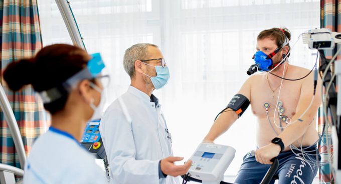 Post Covid Reha Pflegekraft und Arzt sprechen mit Patienten beim Lungenfunktionstest auf dem Ergometer
