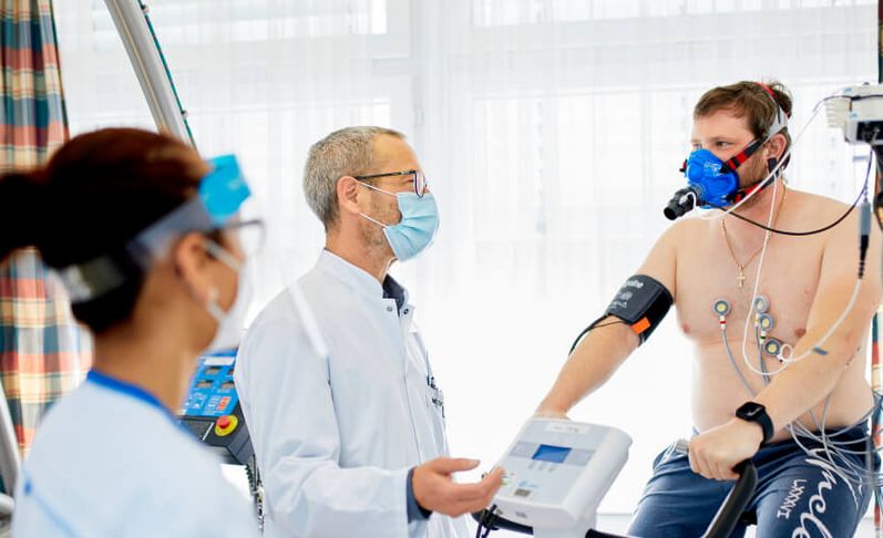 Pflegekraft und Arzt sprechen mit Patienten beim Lungenfunktionstest auf dem Ergometer